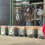 A worker in red safety gear and a white helmet inspects chemical storage containers at a DTBPS application site in a refinery.