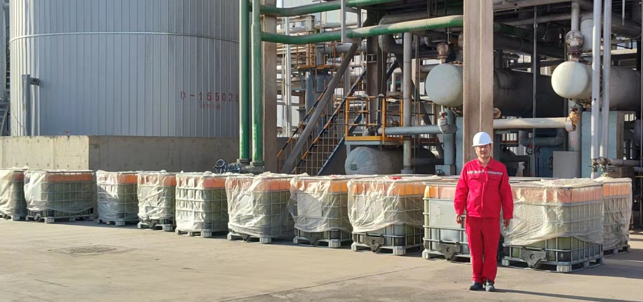 A worker in red safety gear and a white helmet inspects chemical storage containers at a DTBPS application site in a refinery.