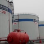 Industrial facility with large Cyclopentane storage tanks labeled V-701, V-702, and V-703, belonging to Junyuan Petroleum Group. Each tank features a blue identification band and access ladders. A red horizontal pressure vessel with piping and valves is visible in the foreground, indicating safety or fire suppression infrastructure. The setting is overcast, with a concrete base and organized layout.
