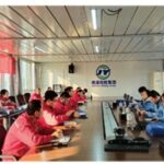 Safety experts and company personnel from Junyuan Petroleum Group gather around a large conference table for a formal safety inspection meeting, with red and blue uniformed teams seated on opposite sides.
