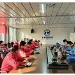 Safety experts and company personnel from Junyuan Petroleum Group gather around a large conference table for a formal safety inspection meeting, with red and blue uniformed teams seated on opposite sides.