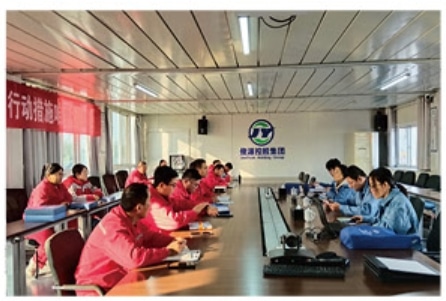 Safety experts and company personnel from Junyuan Petroleum Group gather around a large conference table for a formal safety inspection meeting, with red and blue uniformed teams seated on opposite sides.