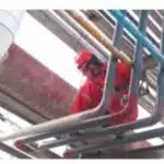 Worker in red protective gear inspecting industrial pipelines for leaks