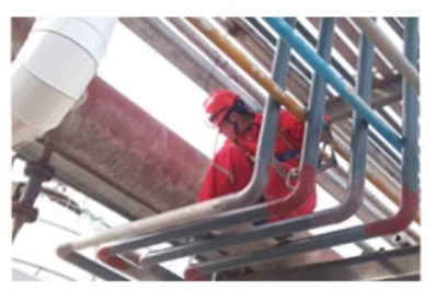 Worker in red protective gear inspecting industrial pipelines for leaks