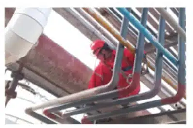 Worker in red protective gear inspecting industrial pipelines for leaks