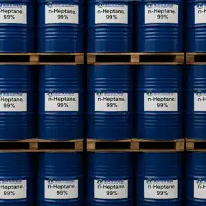Stacked blue metal drums labeled n-Heptane, 99% on wooden pallets in warehouse
