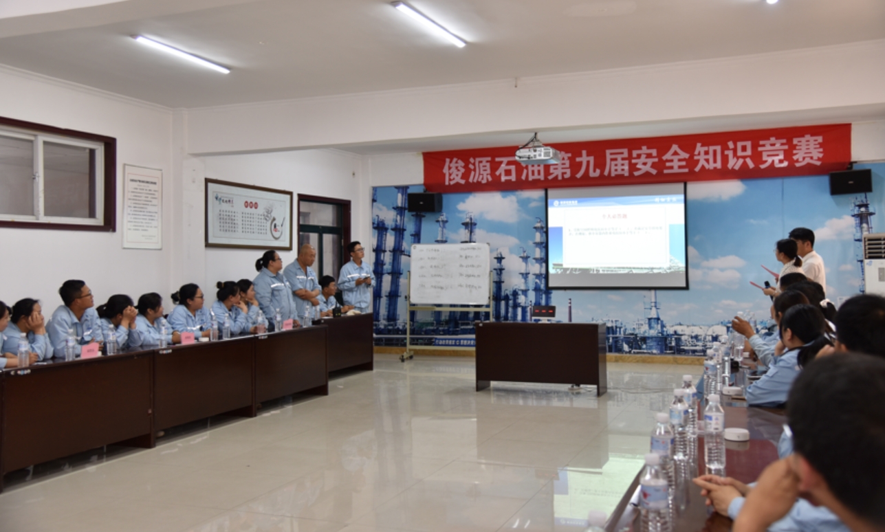 Junyuan Petroleum Group employees participating in the 9th Safety Knowledge Competition in a conference room with a red banner reading Junyuan Petroleum 9th Safety Knowledge Competition in Chinese.