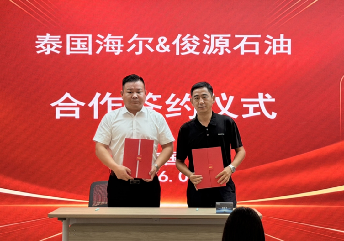 Representatives from Junyuan Petroleum Group and Haier Appliances Thailand holding signed strategic agreement booklets in front of a red backdrop.